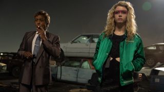 Giancarlo Esposito smokes a cigarette with attitude while Mia Goth stands watching off screen carnage in MaXXXine.