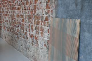 Brick wall with panel displaying striped wallpaper from the living colour project by Buro Belen