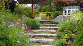 garden with wild planting and rustic garden path leading to outdoor dining area