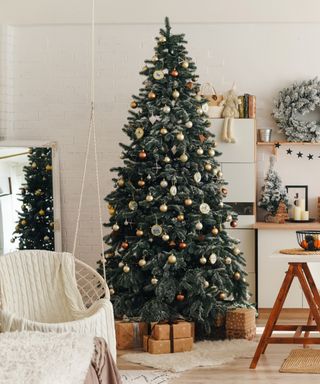 An image of a Christmas tree in a neutral living room with wooden accents and a ceiling anchored swing chair