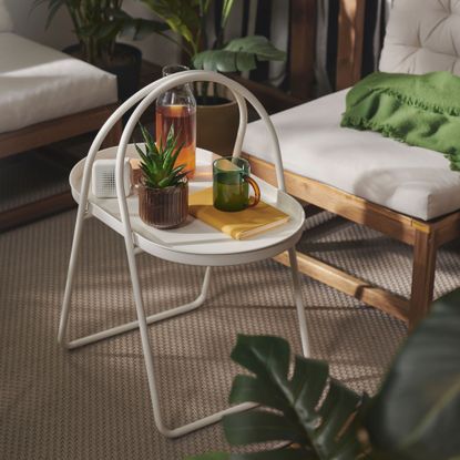 IKEA's white outdoor coffee table on a balcony with a mug, bottle and plant placed on top of it