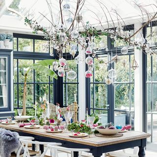 Dining table in conservatory with baubles hanging from branches
