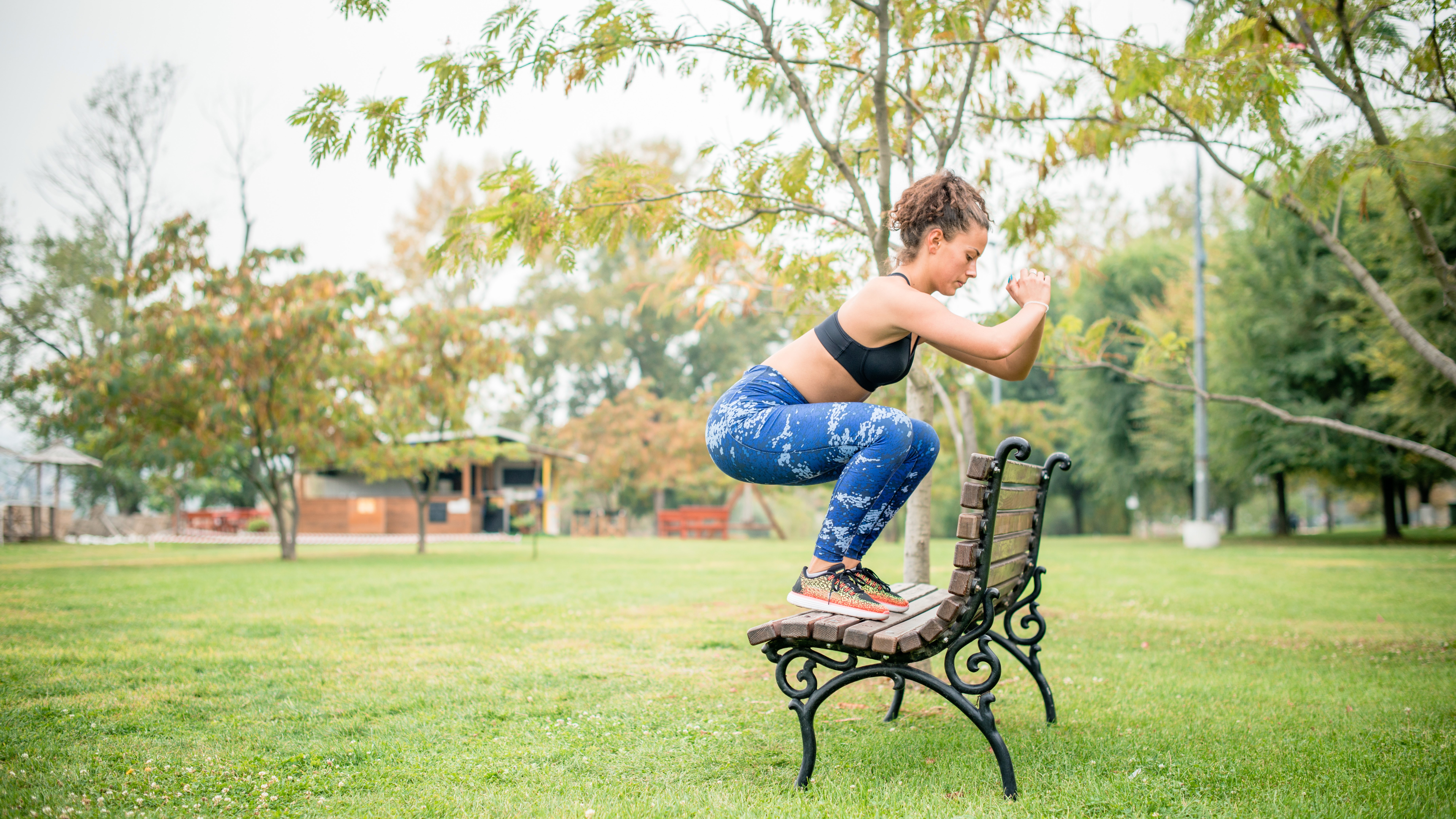 A woman doing a jump squat onto a bench in the park