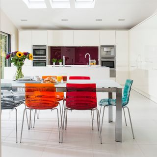 kitchen area with white kitchen units and white dinner table and multicolour chairs