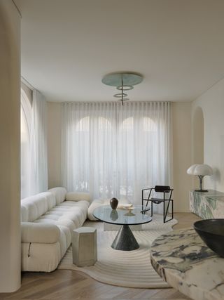 a white living room with a camaleonda sofa and a glass coffee table balanced on a cone base