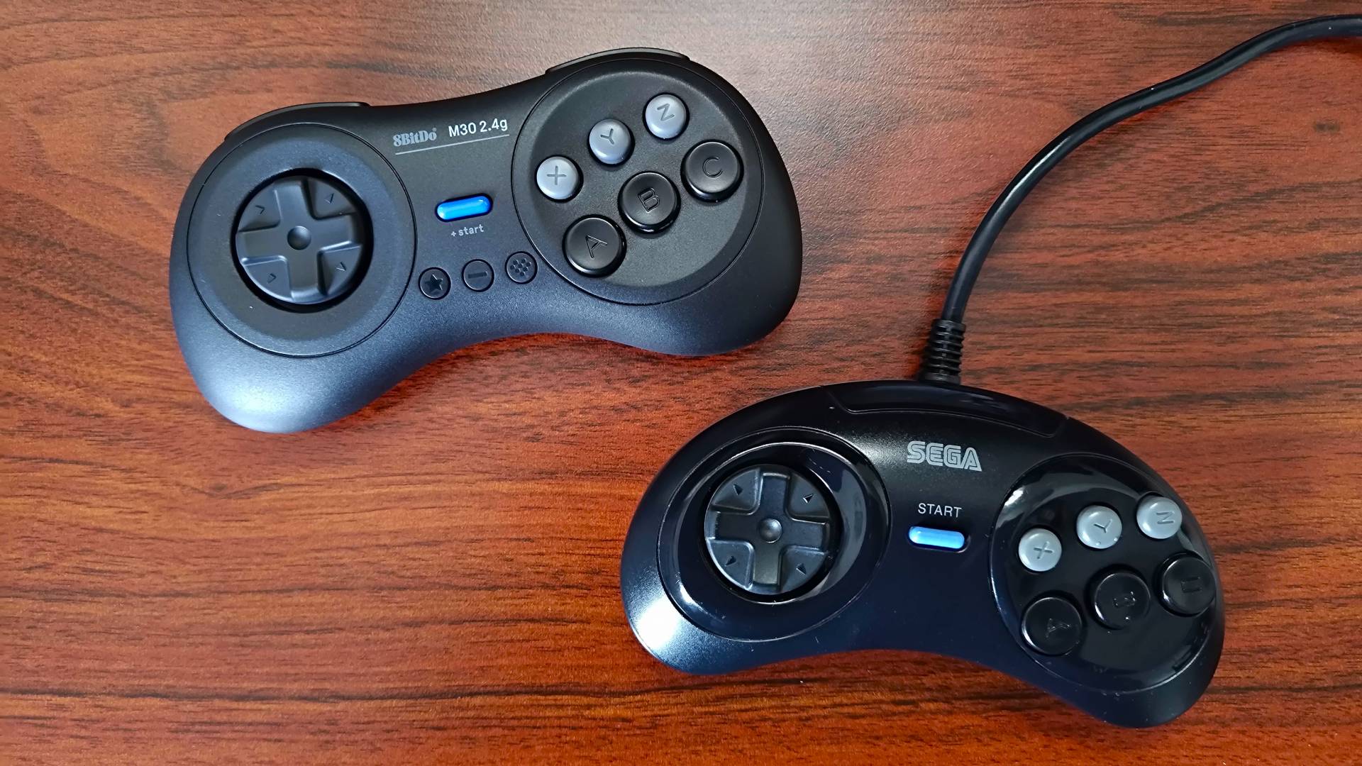 8Bitdo SM30 2.4g controller on top left and original Sega 6 button gamepad on bottom right on woodgrain table.