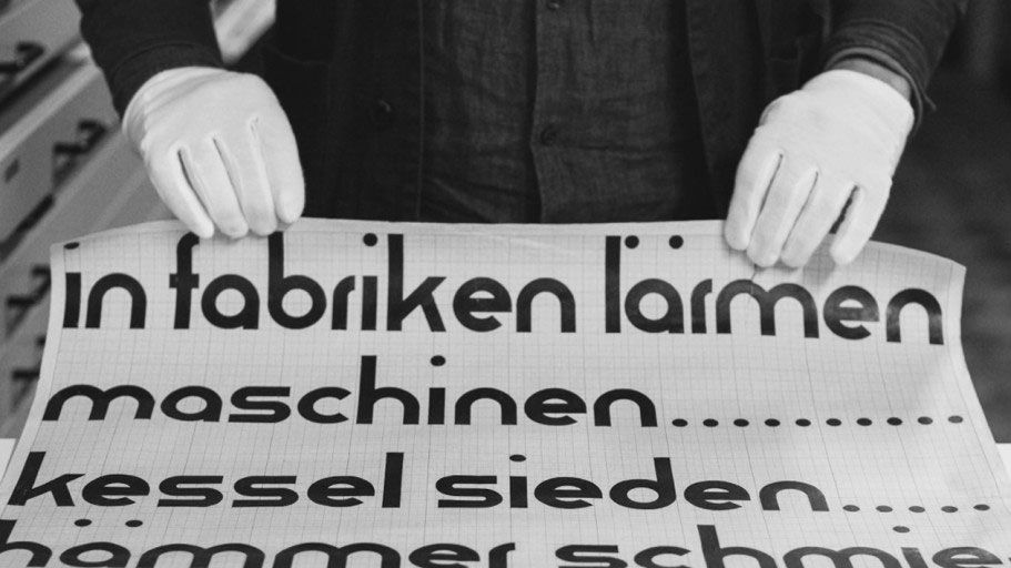 Gloved hands delicately handling a sheet of Bauhaus typography