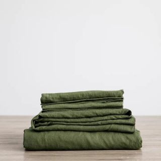 Linen Sheet Set in forest green against a bedroom wall.