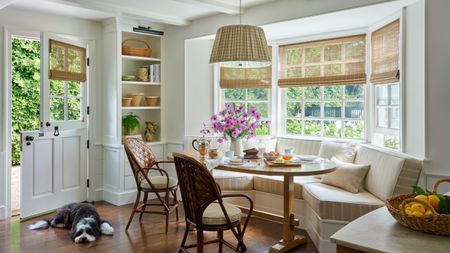 The end of a white kitchen with a large striped banquette installed into a bay window