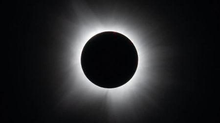 A black circle against a black background surrounded by white wispy tendrils