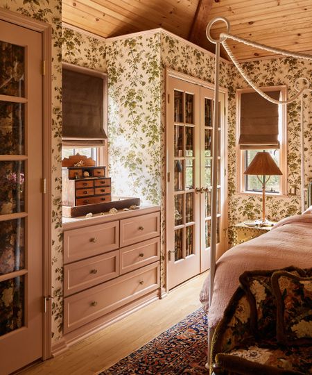 a floral wallpapered bedroom with blush pink built in glass fronted storage and a canopy bed