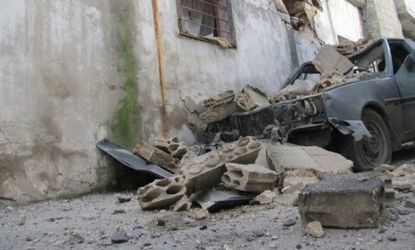 The remains of a wrecked vehicle are seen next to a damaged house in Homs.