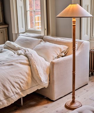 neutral linen sleeper sofa made up for a guest with bedding and a floor lamp