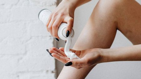 A person spraying shaving foam out of a tube into their hand, with their bare leg up