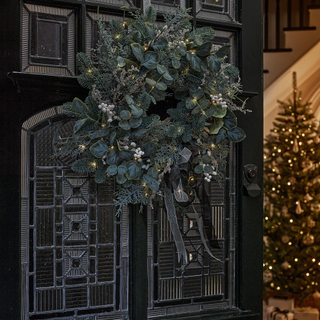 Wreath on a partially open door. A brightly lit Christmas tree is in the background