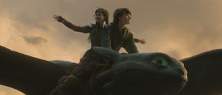 Hiccup (Mason Thames) and Astrid (Nico Parker) riding on Toothless in How To Train Your Dragon