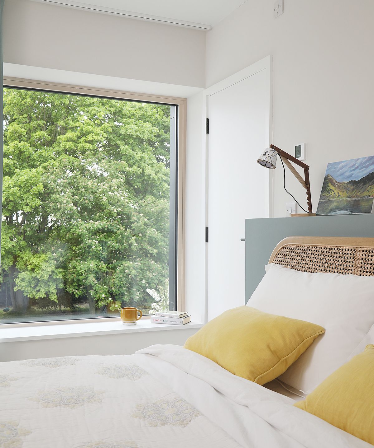 A double bed with yellow throw cushions and a large picture window