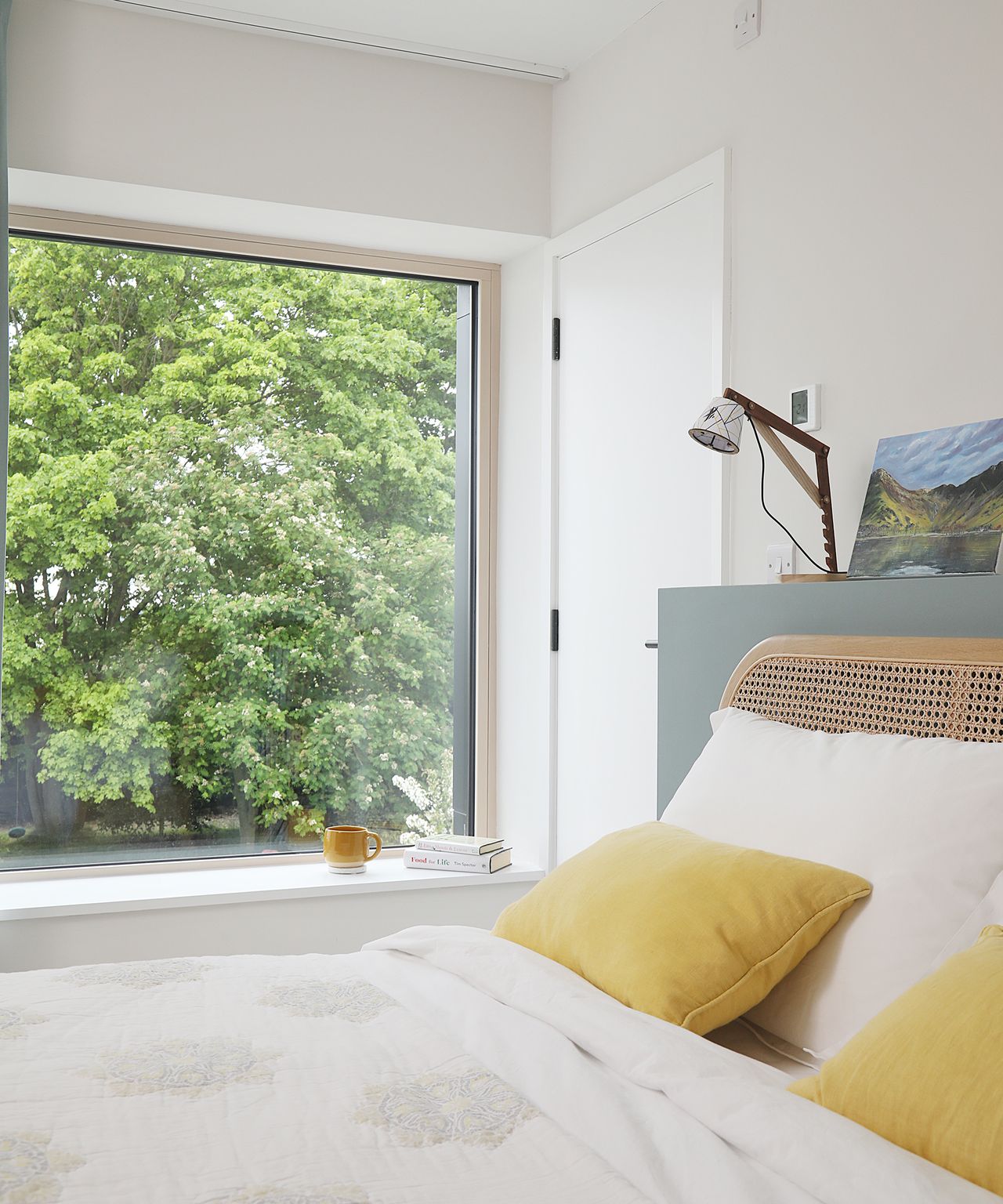 A double bed with yellow throw cushions and a large picture window