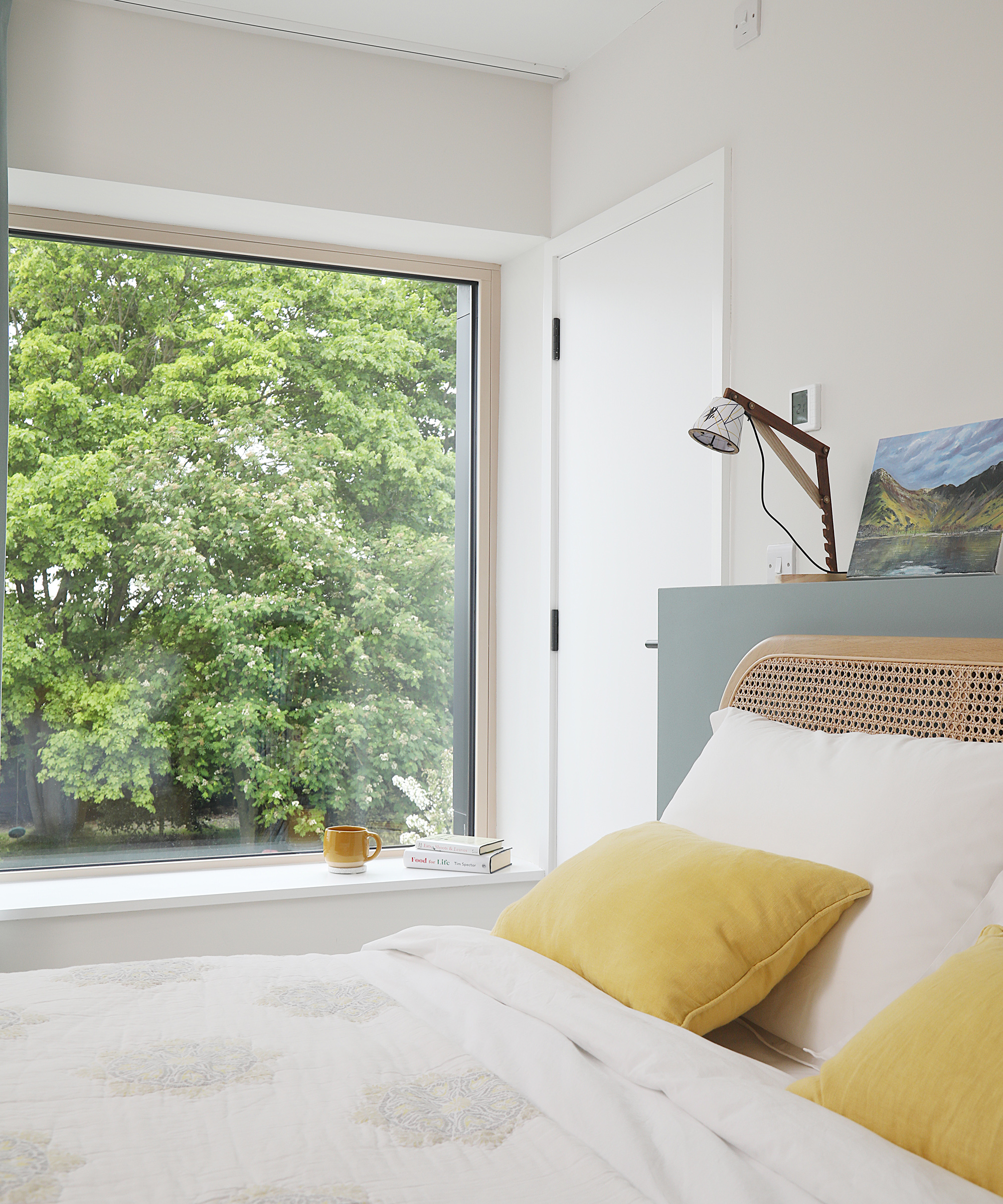 A double bed with yellow throw cushions and a large picture window 