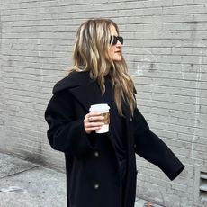 Eliza Huber wearing a black long coat, navy blue sweater, and navy trousers.