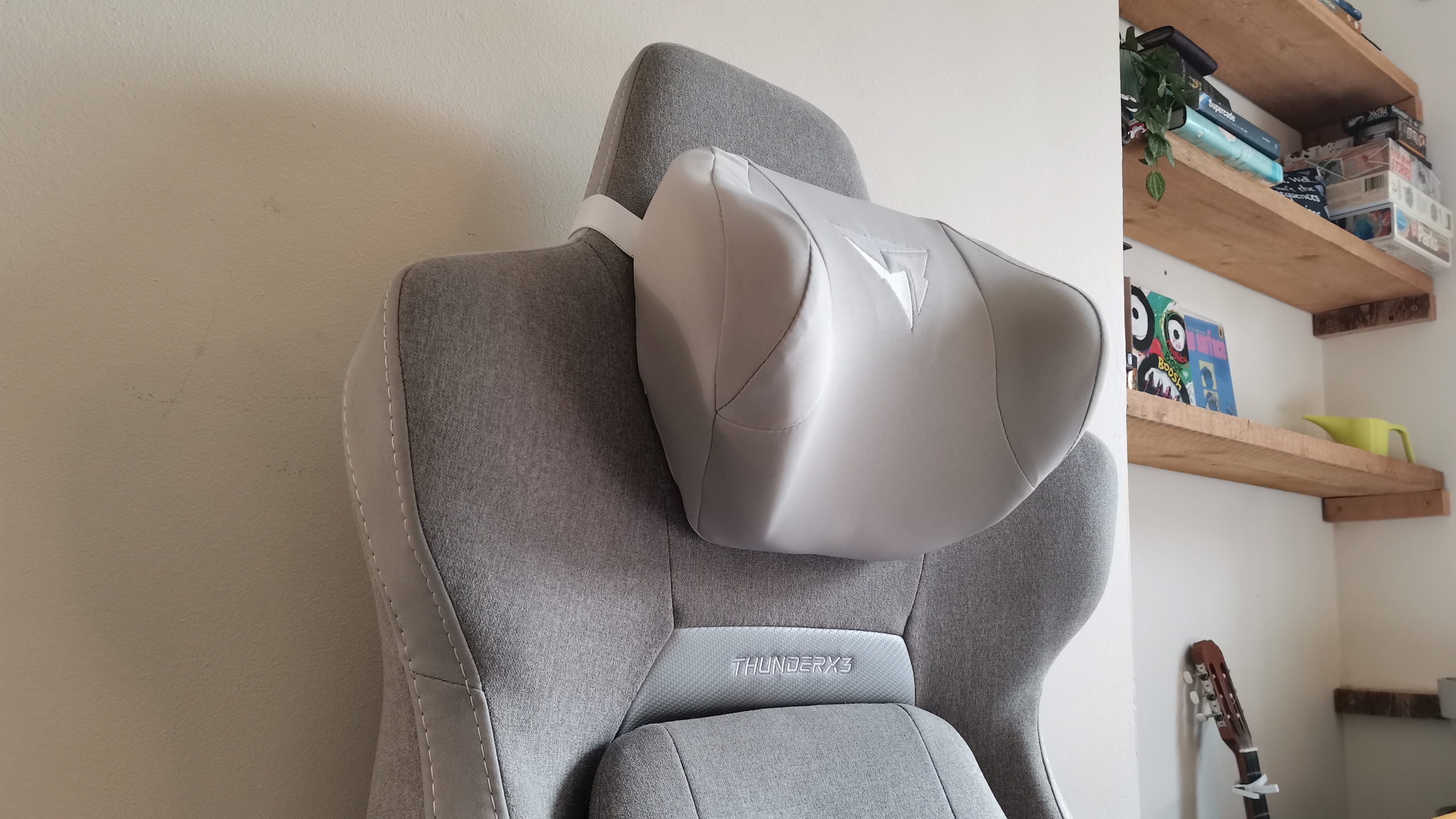 The ThundercoreX3 Core gaming chair in grey in front of a pale wall, next to a wooden bed frame