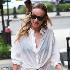 Olivia Wilde wearing a sheer white button-down with an ivory Aritzia lace-trimmed slip skirt and flat black loafers