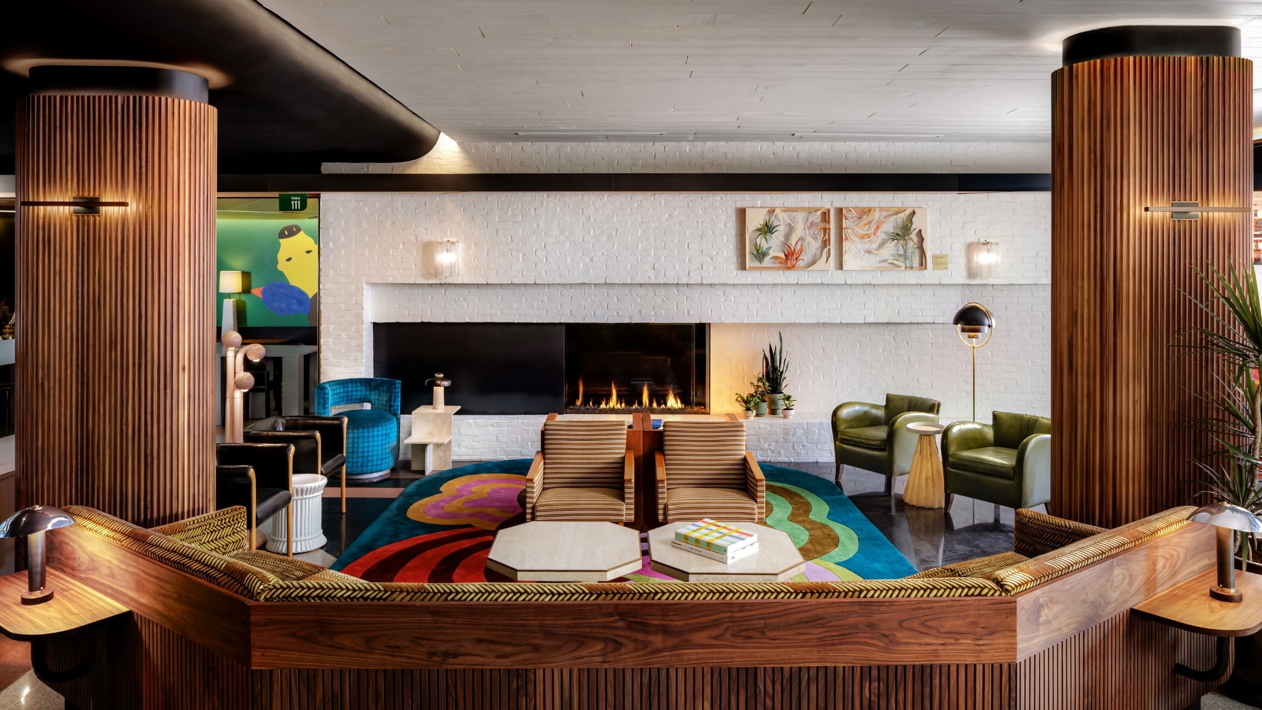  hotel lobby carved from texture wood, with colorful rugs and artworks, white-washed walls, and a lit fire place.