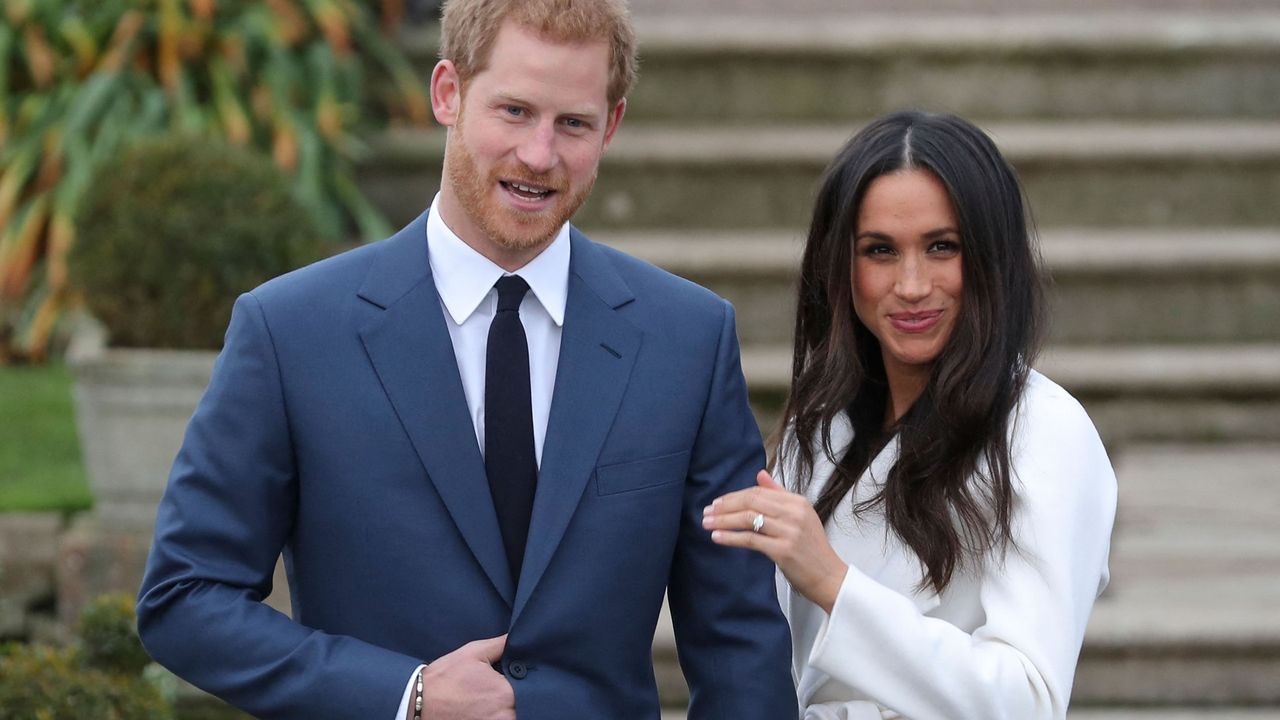 Britain&#039;s Prince Harry stands with his fiancée US actress Meghan Markle as she shows off her engagement ring whilst they pose for a photograph in the Sunken Garden at Kensington Palace in west London on November 27, 2017, following the announcement of their engagement. - Britain&#039;s Prince Harry will marry his US actress girlfriend Meghan Markle early next year after the couple became engaged earlier this month, Clarence House announced on Monday.