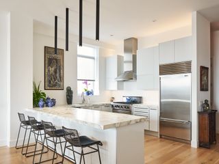 A white minimalist kitchen with tube lighting over a peninsula kitchen island