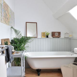 Bathroom with white bathtub and light grey wall panelling shelf with trinkets