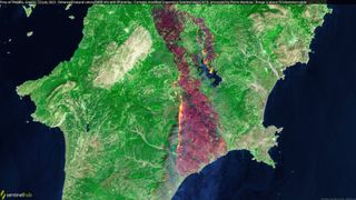 A satellite image above the Greek island of Rhodes, with a central portion scared with dark red and black from wildfire