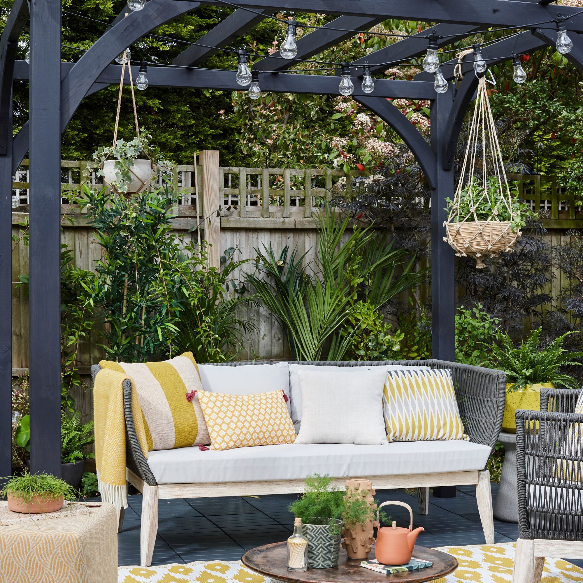 Outdoor seating area with cushions beneath wooden pergola with festoon lights