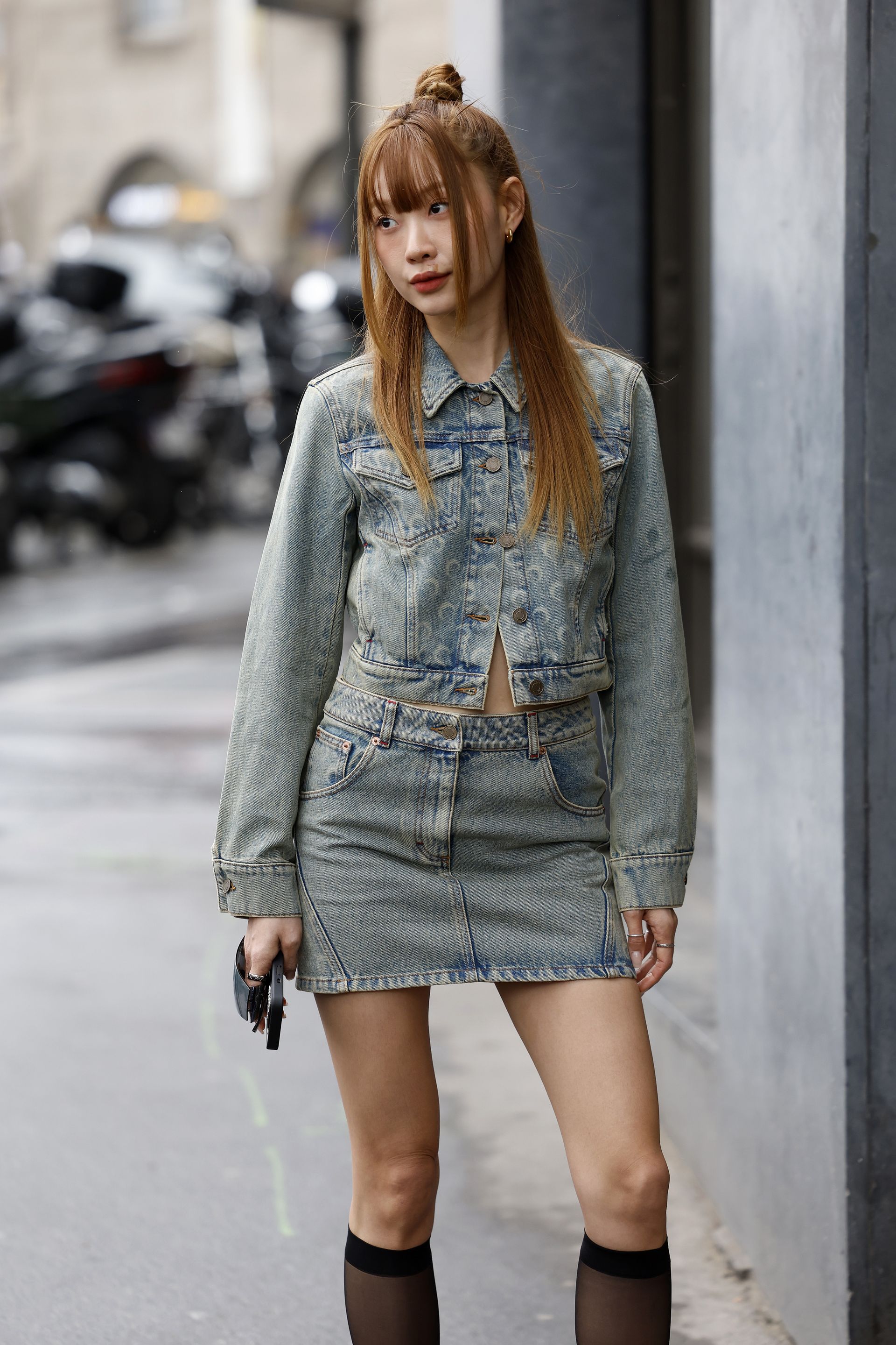 A woman wearing a denim jacket, and a denim mini skirt
