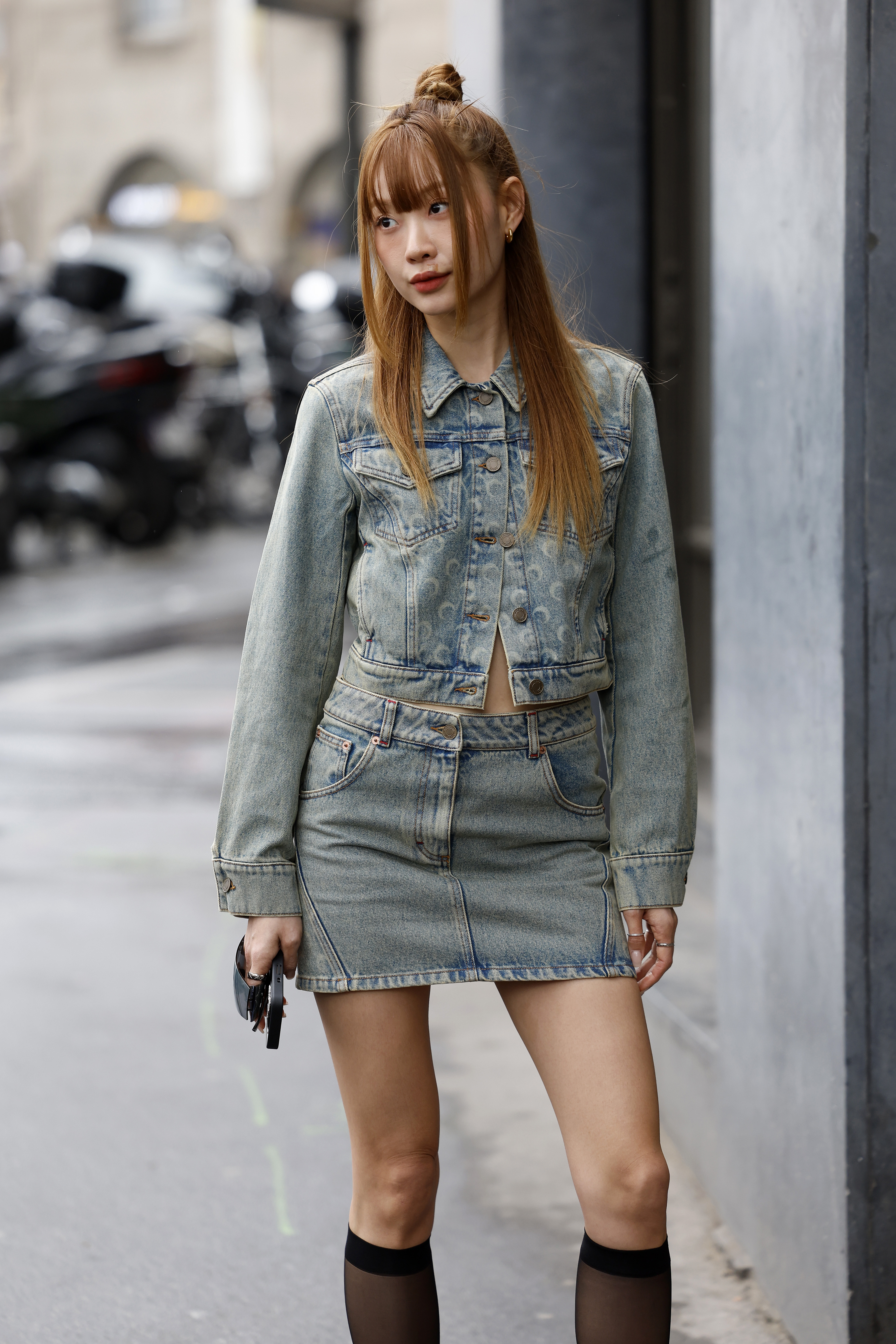 A woman wearing a denim jacket, and a denim mini skirt