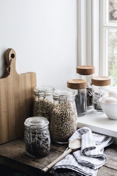 selection of storage jars filled with nuts, lentils and other dried goods on kitchen surface by The White Company