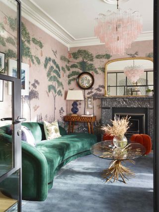 green curved sofa in a living room with pink muralled wallpaper and dark blue rug