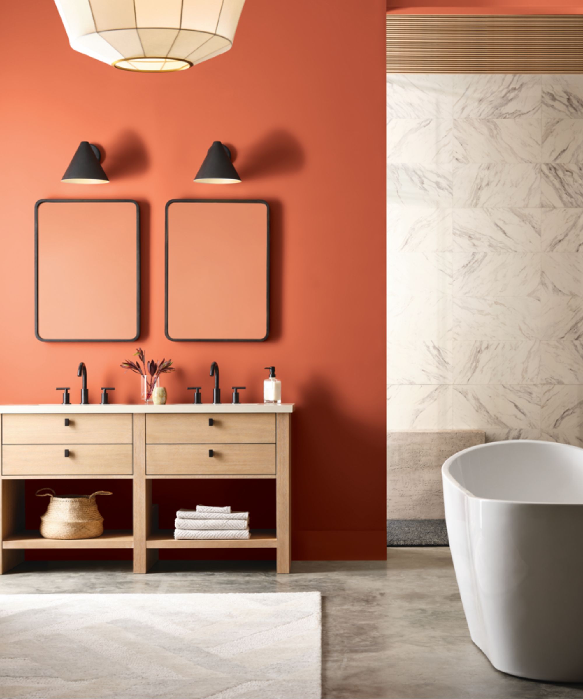 a modern bathroom painted in Sherwin Williams terracotta paint shade: Pennywise with black mirrors and sconces, a freestanding tub, and a double oak vanity