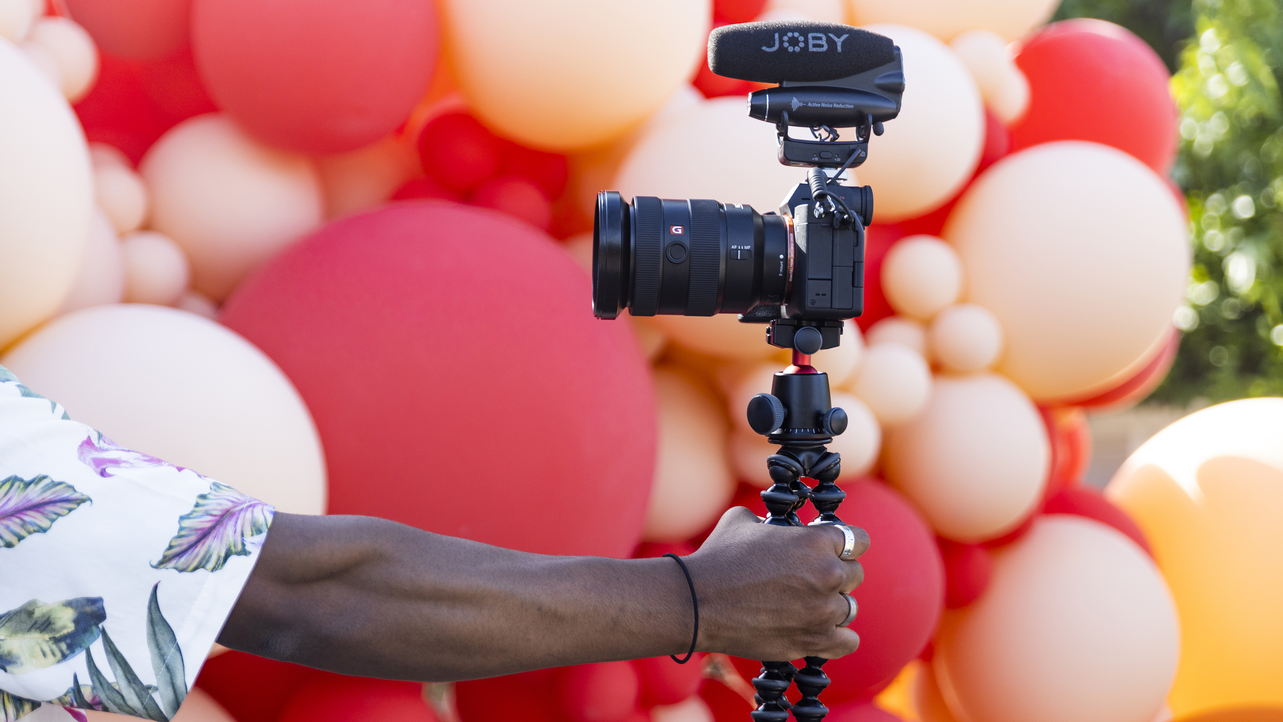 A hand holding a camera with a Joby Wavo microphone on top