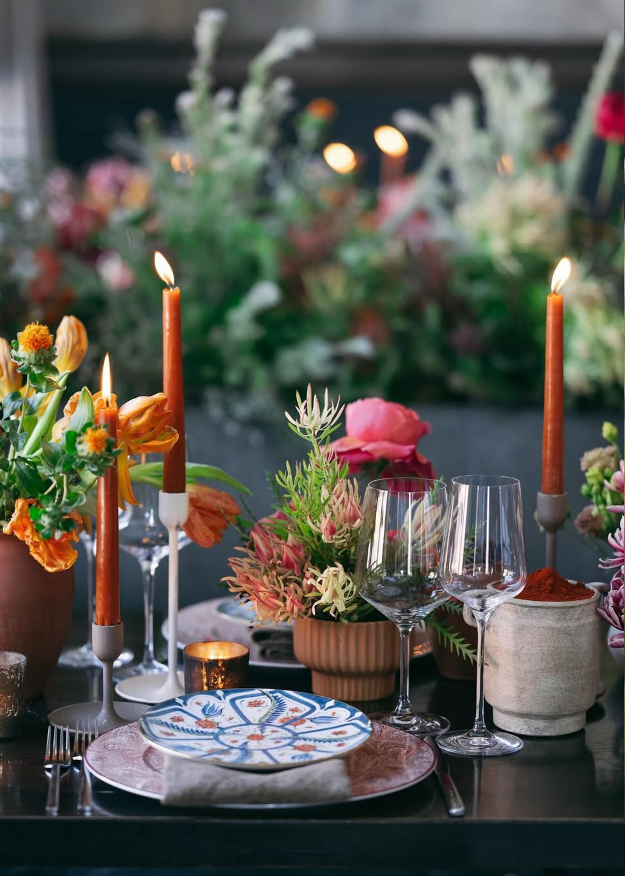 A dining table with high-low decor, plates, wine glasses and candles