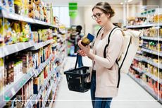 woman looking at a box label while carrying a basket in a supermarket