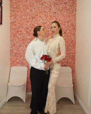 Gabby Windey in a lace wedding dress standing with Robby Hoffman holding a red bouquet