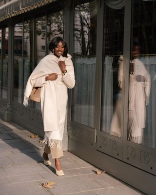 Woman wearing white coat with fringe, walking down Paris street.