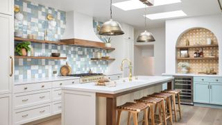 kitchen with cream units long narrow island and open wall shelves with green blue and white tiled backsplash