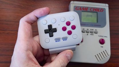 Hand holding 8Bitdo FlipPad mobile controller with Game Child knock off Game Boy in backdrop.