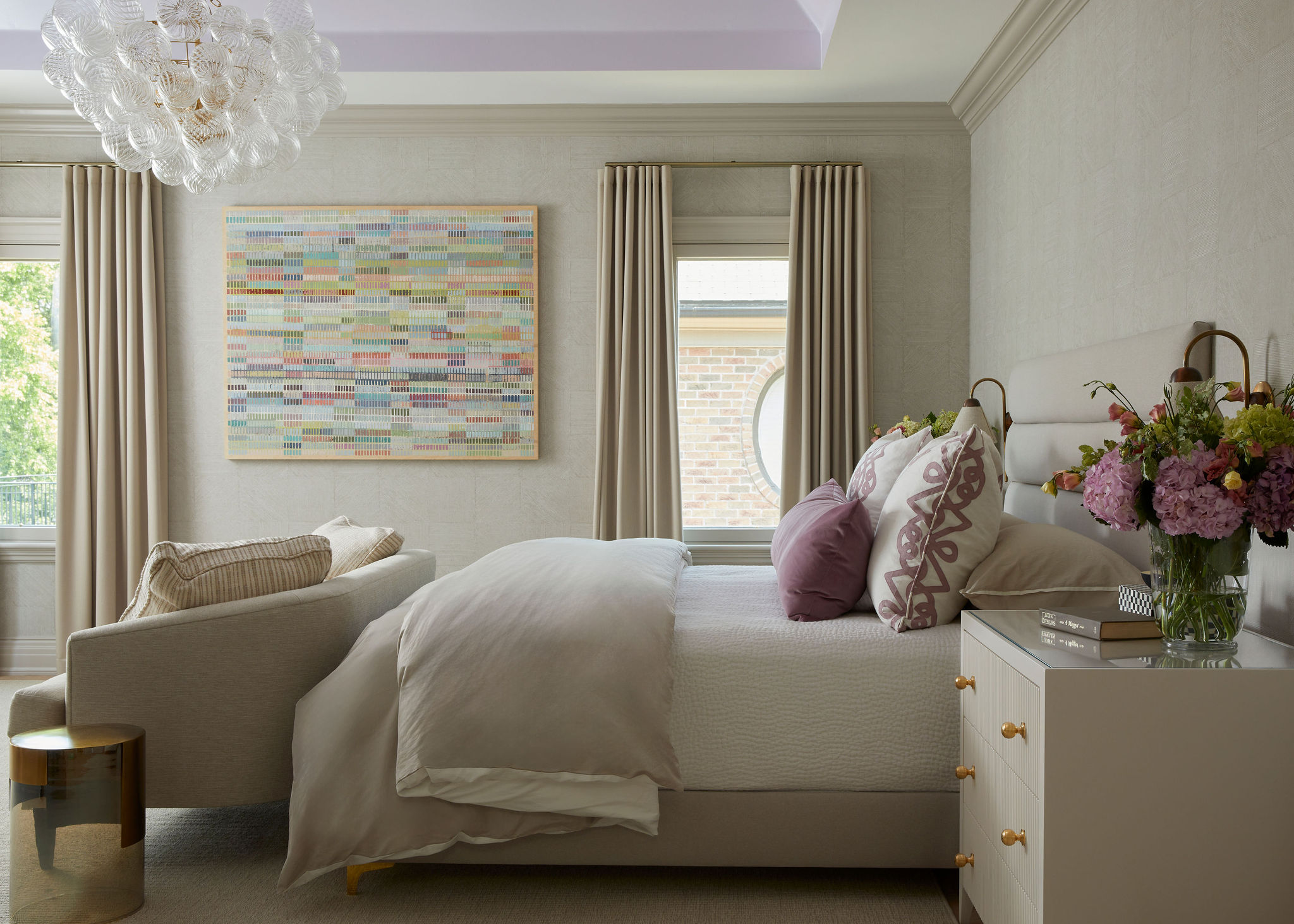 A neutral bedroom with light touches of lavender across the ceiling and on pillowcases.