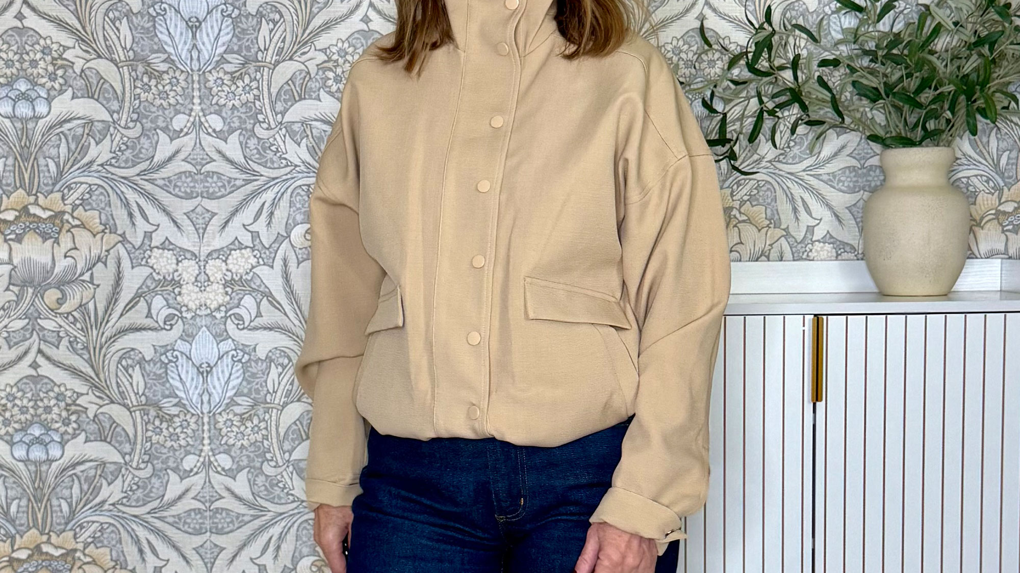 A woman wearing a tan funnel-neck jacket and jeans.