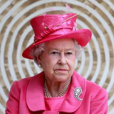 Queen Elizabeth wearing a bright pink coat and hat in front of a circular patterned wall