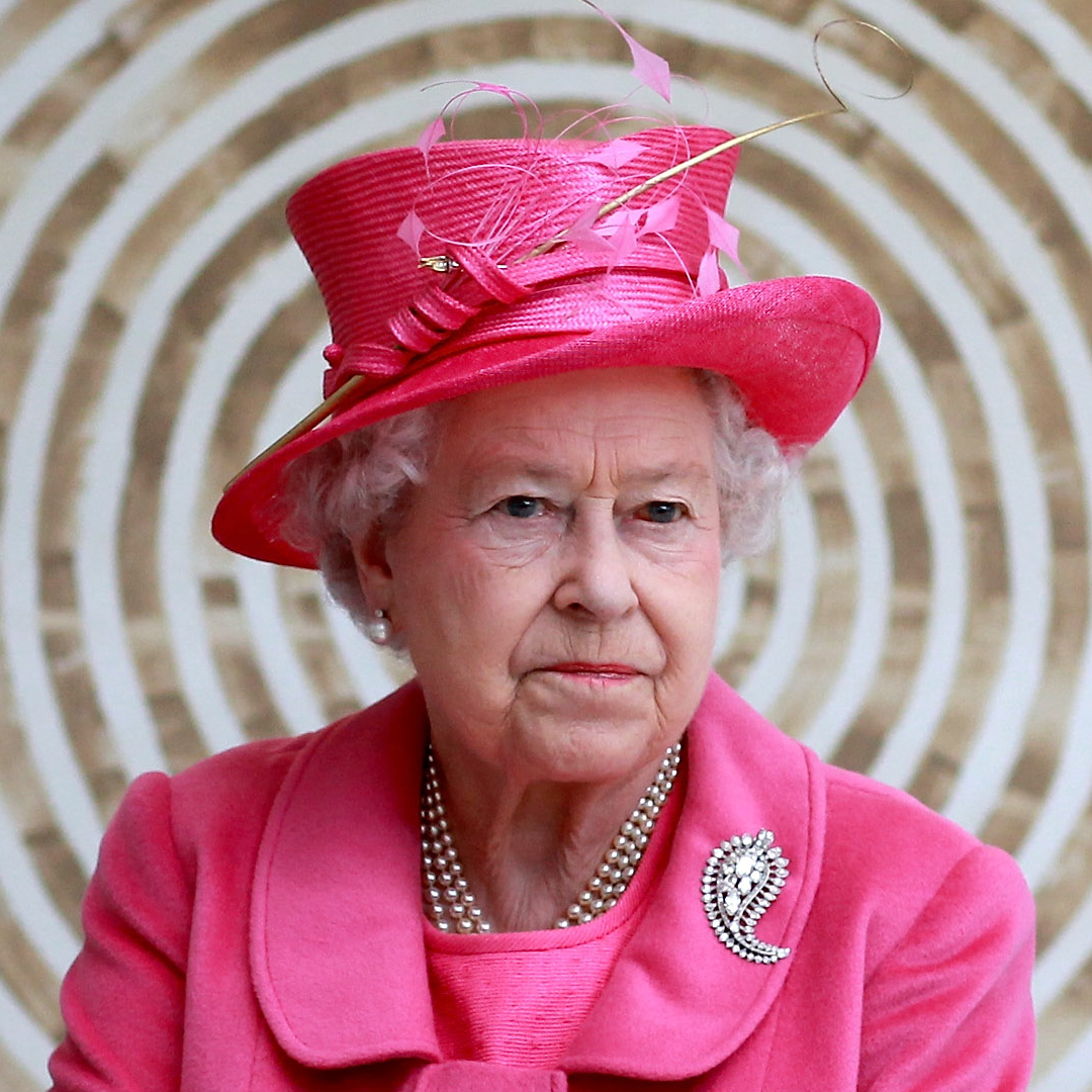 Queen Elizabeth wearing a bright pink coat and hat in front of a circular patterned wall