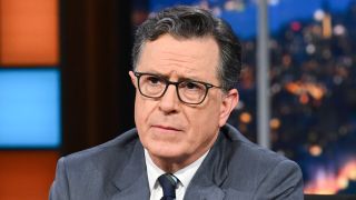 Stephen Colbert stern-faced behind desk on The Late Show with Stephen Colbert