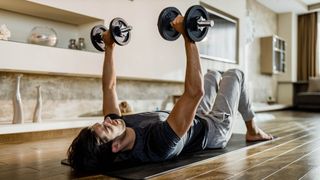 Man performs floor press chest exercise with dumbbells at home